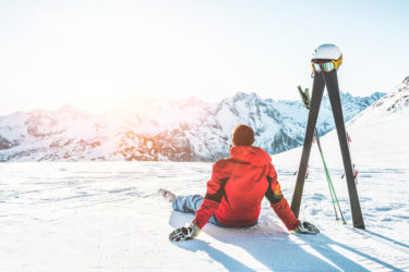 Man sitting next to ski poles looking at mountains