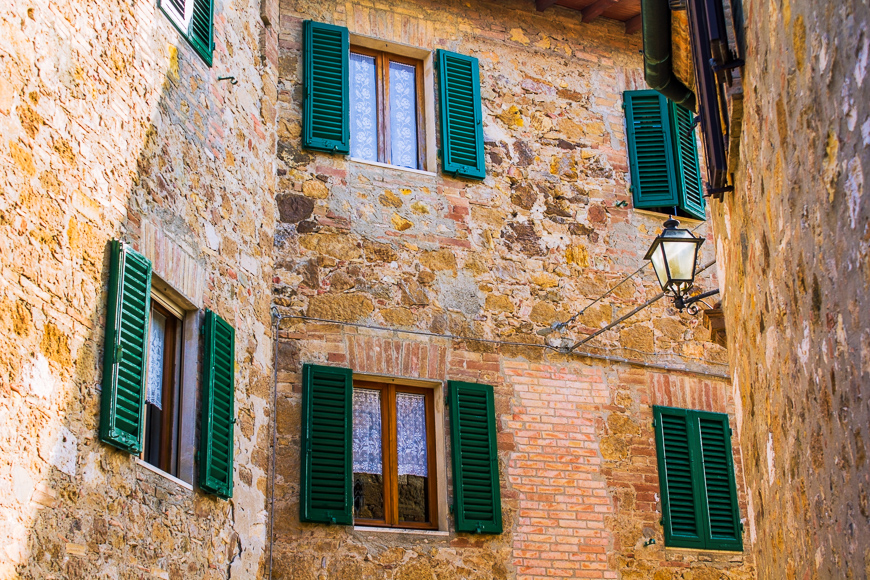fragment of a brick wall of an old historical town in Italy with windows with green wooden shutters and a sunlit street lamp